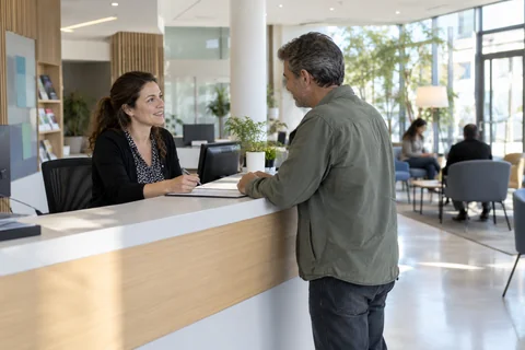 Une agente accueille un visiteur dans un service public local fictif.