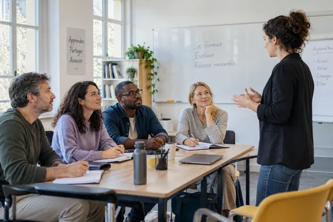Une formatrice échange avec quatre adultes autour d’une table de formation.